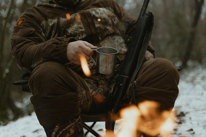男人坐在篝火与咖啡和枪