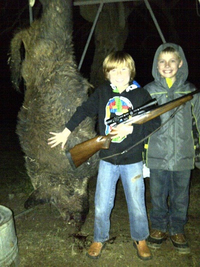 孩子们拿着步枪站在死猪旁边