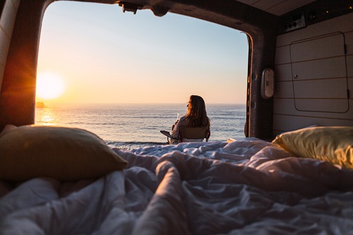 女人欣赏日落的观点而坐在椅子上露营车在沙滩上